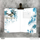 Open notebook with blue splatter design and bird illustration on a gray background, featuring the brand 'Arden Creative Studio'.