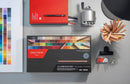 Crayon set with color swatch, red notebook, and other stationery items on a gray surface