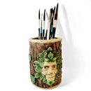 Tree stump-shaped pen holder with face design holding paintbrushes on a white background