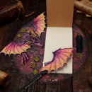 Decorative dragon wings on a notebook with a pen, on a wooden surface.