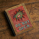 Decorative book with 'Do Not Open' embossed on the cover, featuring a dragon design, on a wooden surface.