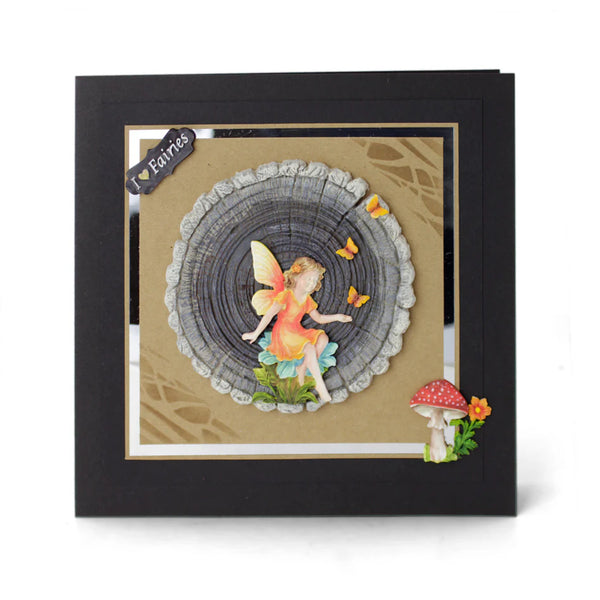 Framed artwork of a fairy sitting inside a tree stump with mushrooms and flowers.