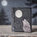 Decorative book with wolf and moon design on a wooden surface with a blurred forest background
