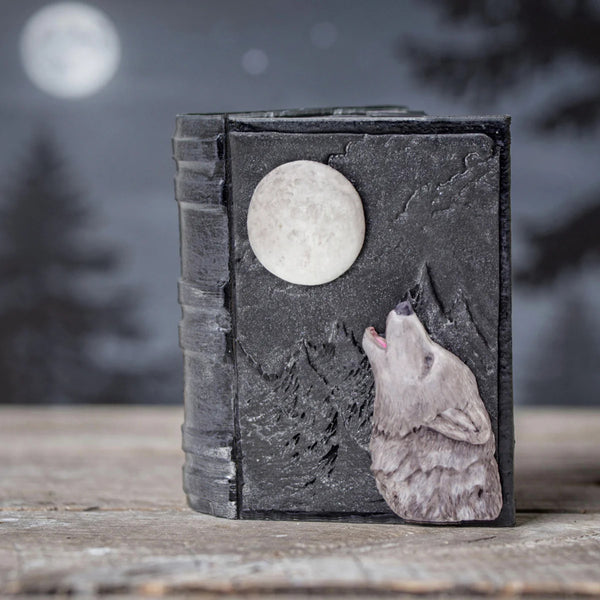 Decorative book with wolf and moon design on a wooden surface with a blurred forest background