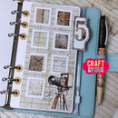 Planner with decorative cover featuring stamps and a camera design, next to a pen on a wooden surface.