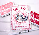 Card with raccoon illustration and 'HELLO' text, surrounded by Gina K. Designs products on a white background