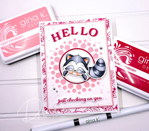 Card with raccoon illustration and 'HELLO' text, surrounded by Gina K. Designs products on a white background