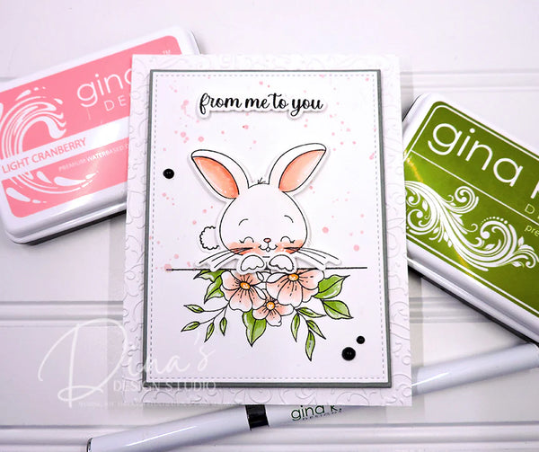Card with a bunny and flowers design, surrounded by Gina K. products on a white background