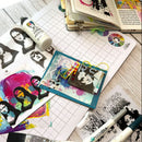 Artistic craft materials including stencils, markers, and a card on a grid surface.