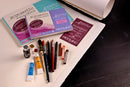 Art supplies including watercolor books, brushes, and tubes on a table.