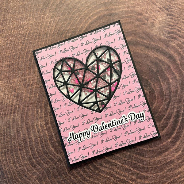 Valentine's Day card with geometric heart design on a pink background with 'I Love You!' text, placed on a wooden surface.