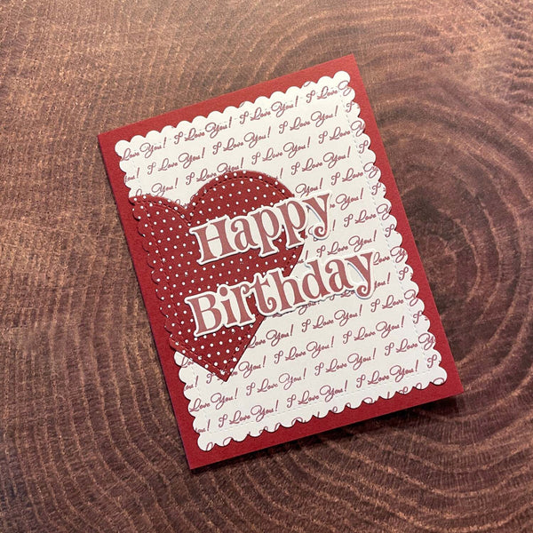 Red birthday card with heart design and 'Happy Birthday' text on a wooden surface
