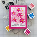 Card with pink flowers and 'blooming with happiness for you' text, surrounded by stamping supplies on a grid background.