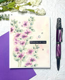 Floral card with 'Thinking of You' message, purple pen, and purple envelope on textured white background