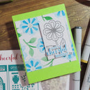 Card with floral design and 'Have a cheerful birthday!' text on a wooden surface with markers.