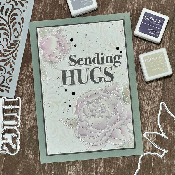 Card with 'Sending Hugs' text and floral design on a wooden surface with craft supplies.