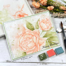 Handmade birthday card with floral design and watercolor effects, surrounded by flowers and art supplies.