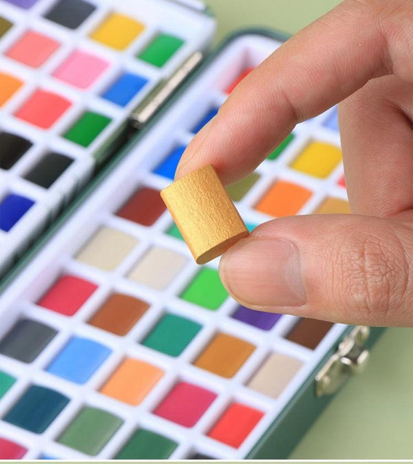 Hand holding a watercolor paint brush over a set of watercolor paints with a close-up view.