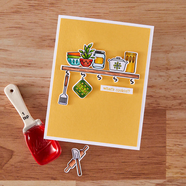 Card with kitchen-themed illustrations on a wooden surface with a red measuring spoon.