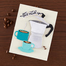 Card with coffee-themed design featuring a percolator and cups on a wooden surface with coffee beans.