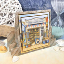 Framed artwork of a fishing shop with decorative elements on a table.
