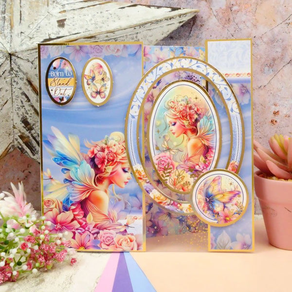 Colorful greeting card with fairy design on a decorative surface with flowers and a plant.