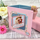 Decorative card with vintage-style illustration and text, placed on a textured surface with flowers and plants.
