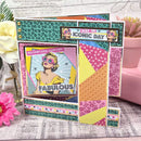 Colorful card with patterned design and text on a textured surface with flowers and a plant.