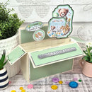Decorative baby gift box with teddy bear design and 'Congratulations' message, surrounded by plants and buttons.