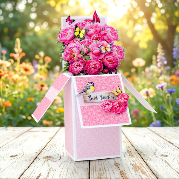 Pink gift box with flowers and decorative elements on a wooden surface with a garden background