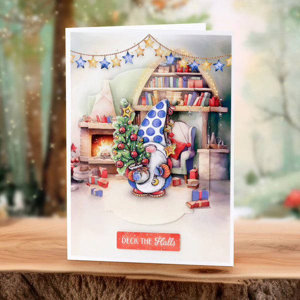 Christmas-themed greeting card with a gnome, tree, and fireplace on a wooden surface.