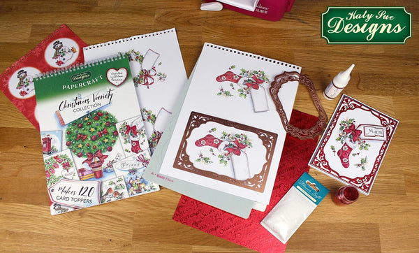 Katy Sue Designs craft supplies on a wooden surface, including cardstock and embellishments.