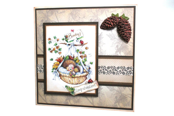 Decorative card with teddy bear, basket, and pinecones on a textured background