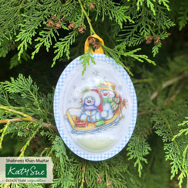 Decorative Christmas ornament with two snowmen on a tree branch, featuring Katy Sue branding.