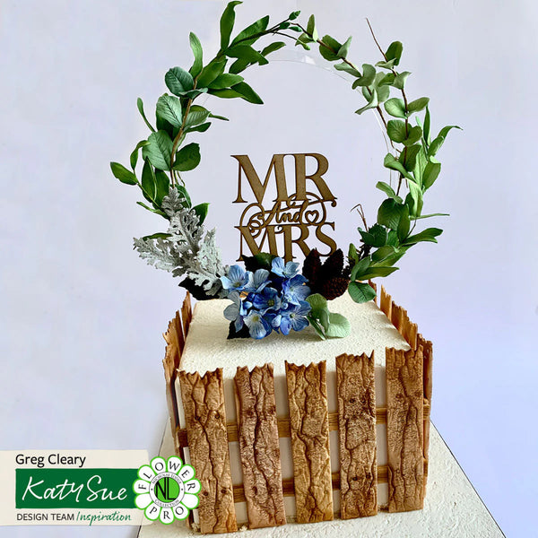 Decorative cake topper with 'MR & MRS' and floral elements on a white background