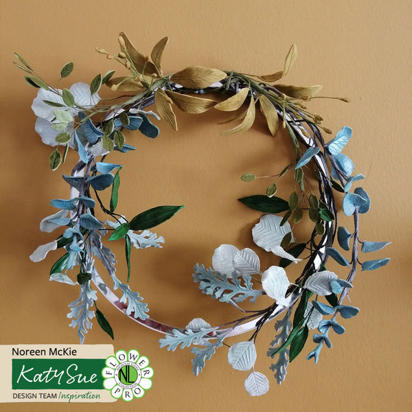 Floral wreath with green and white leaves on a beige background, featuring Katy Sue Design branding.