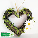 Heart-shaped wreath with green leaves and a white flower on a white background, featuring Katy Sue Design Team logo.