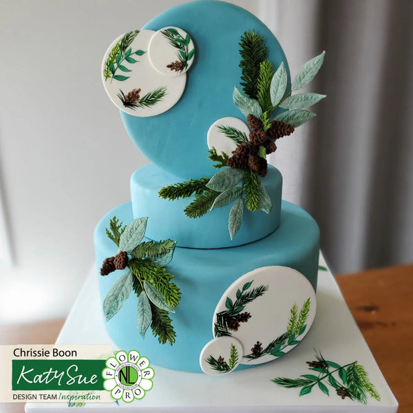 Two-tiered blue cake with floral decorations on a white surface.