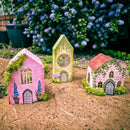 Three miniature fairy houses with greenery against a natural background