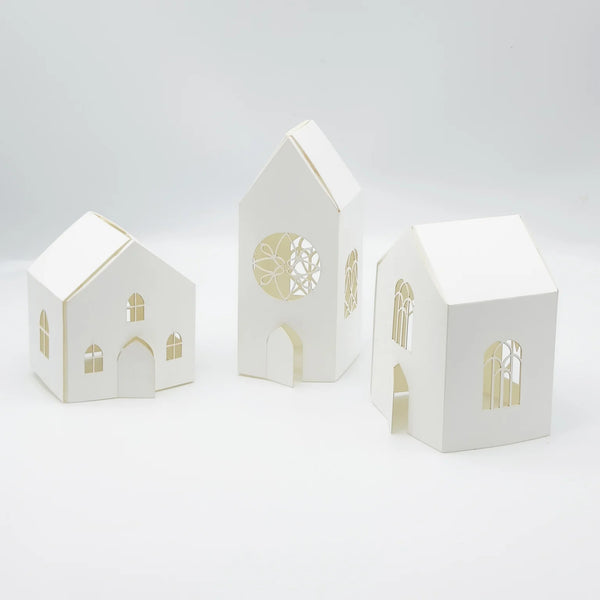Three white paper house models with cut-out windows and doors on a light gray background