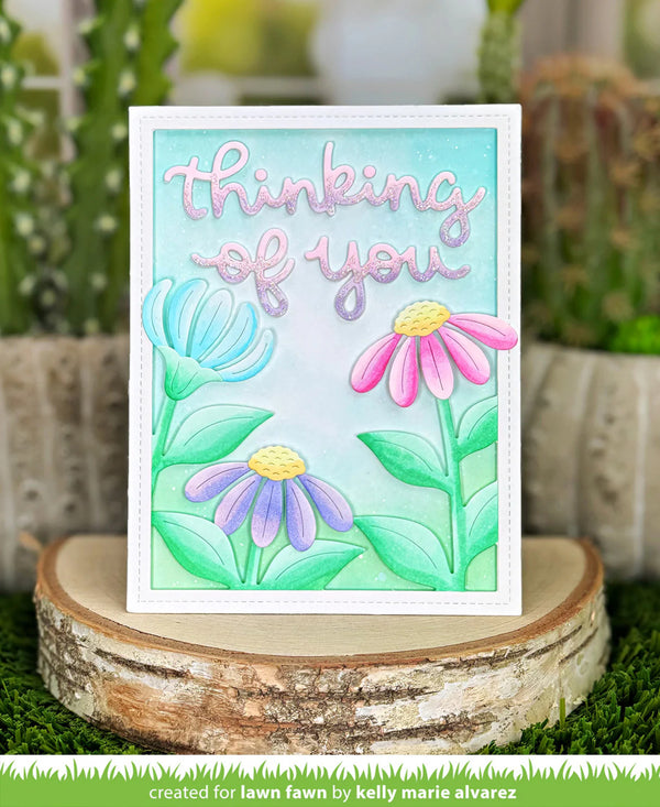 Card with flowers and 'thinking of you' text on a wooden stand with plants in the background