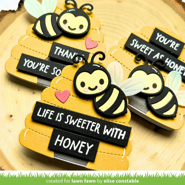 Three decorative bee-shaped items with text on a wooden background