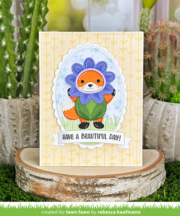 Card with a cute fox character in a flower costume on a wooden stand with plants in the background