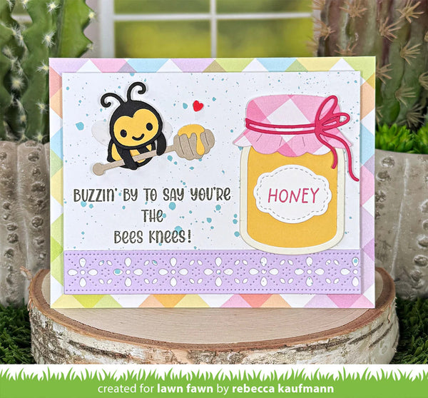 Card with bee and honey jar design on a wooden block with plants in the background