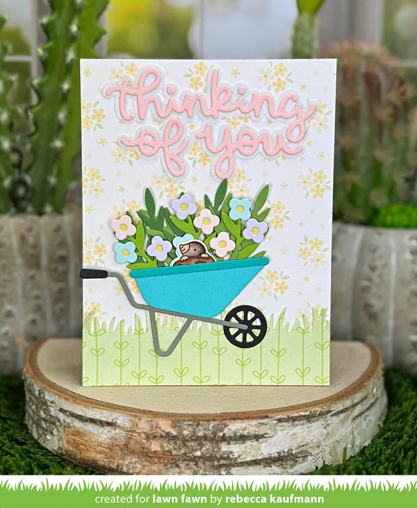 Greeting card with 'thinking of you' text, flowers, and a wheelbarrow on a decorative stand.