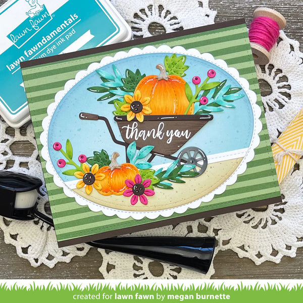 Card with a wheelbarrow of pumpkins and flowers on a green and white striped background, surrounded by crafting supplies.