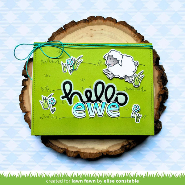 Green pouch with sheep design and 'hello ewe' text on a wooden log with grass background