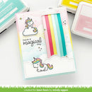 Card with unicorn design and text 'have a magical day' surrounded by stamping supplies on a white background.