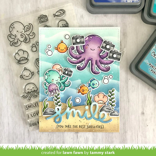 Card with cartoon octopus and fish design, surrounded by stamp set and ink pads on a wooden surface.