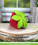 Red strawberry-shaped object with green leaves on a wooden surface